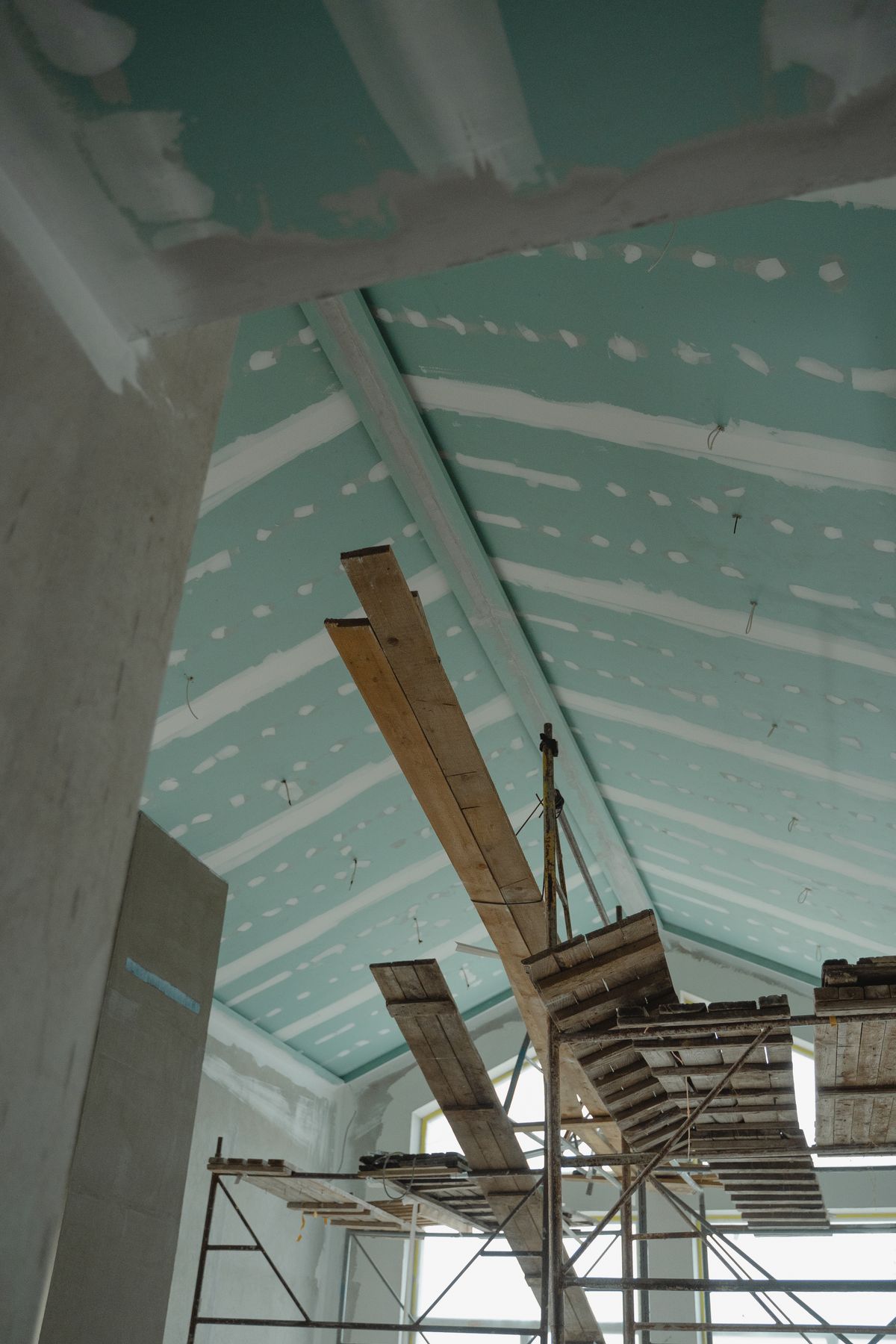 A boarded drywall ceiling with taped seams over scaffolding