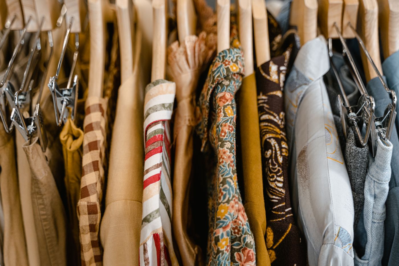 A rack of printed and patterned designer fabrics on wooden hangers, warm light