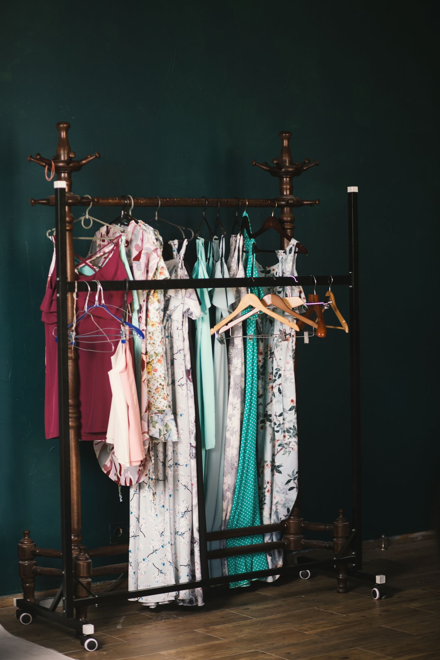 A vintage wooden rack hung with designer garments against a deep teal wall