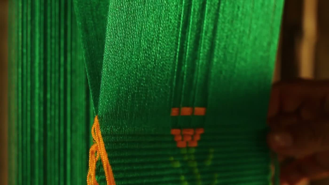 Vivid green and orange threads strung on a weaving loom