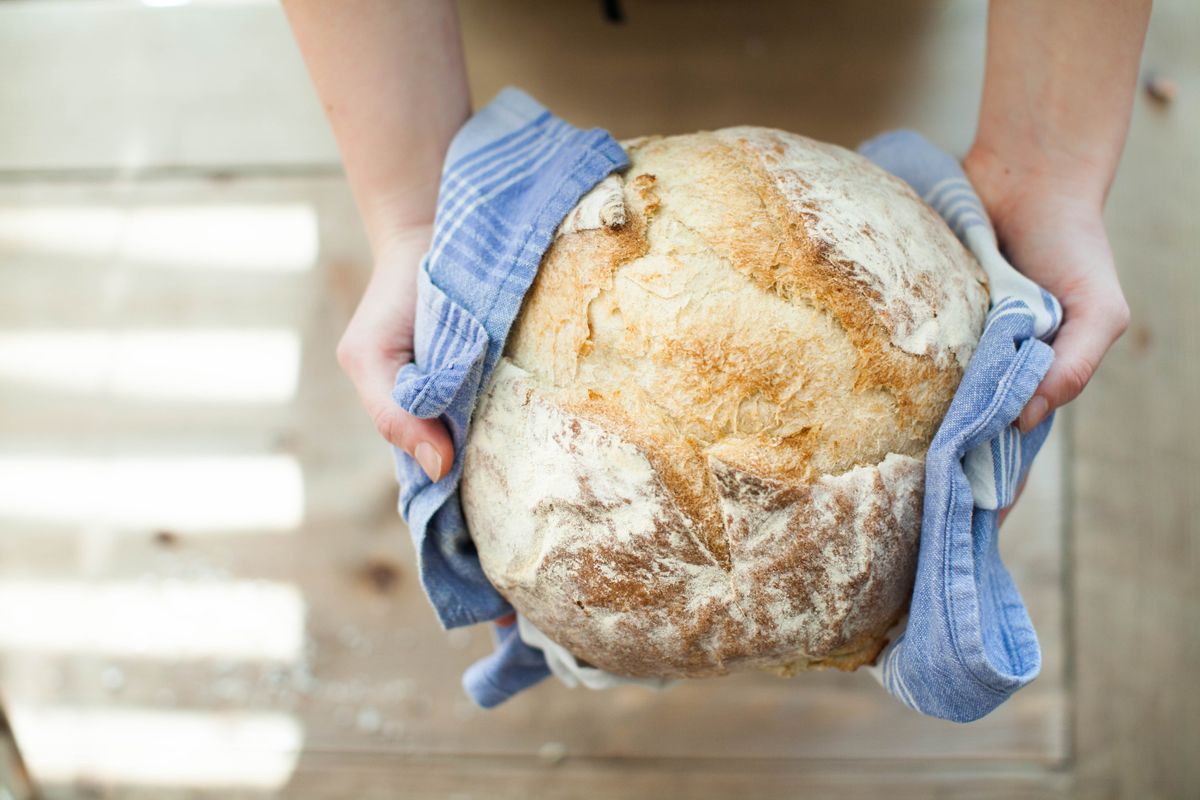 Hands holding a round artisan loaf wrapped in cloth