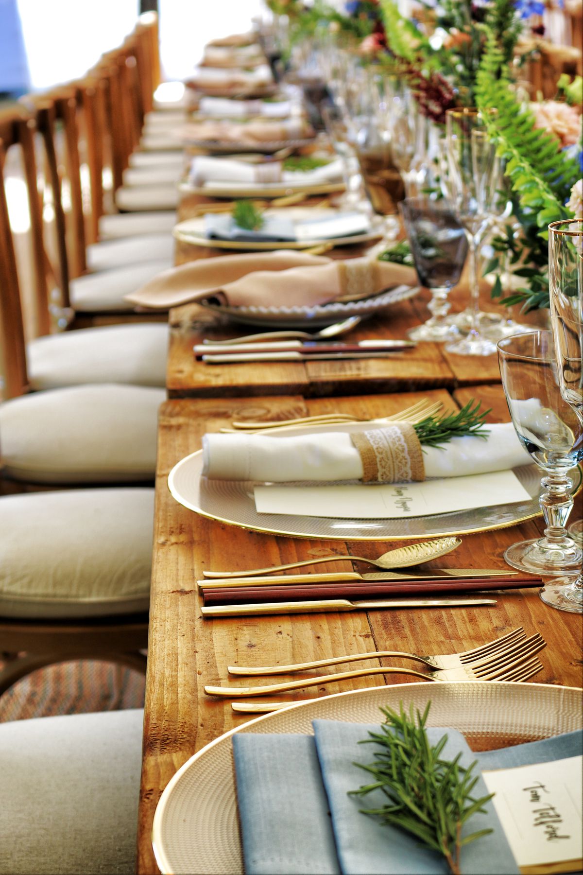 A long catering table set with linens, glassware and rosemary sprigs