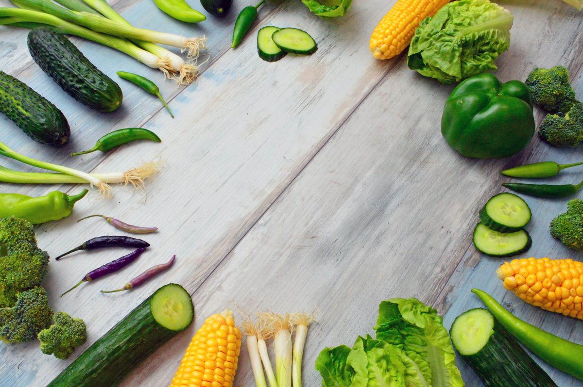 A border of fresh green vegetables on a whitewashed wooden table