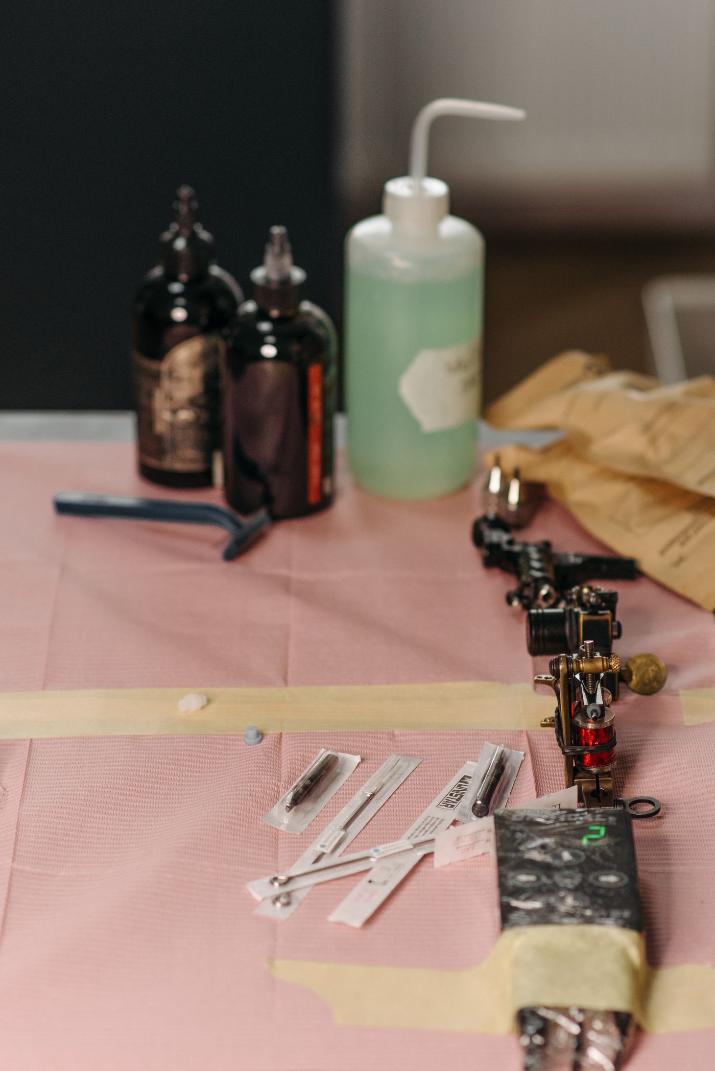 A tattoo machine, wrapped needle bars and squeeze bottles laid out on a covered workstation
