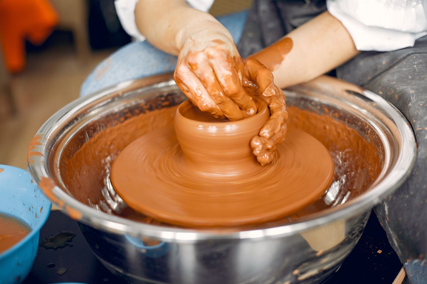 Hands throwing wet clay on a spinning wheel