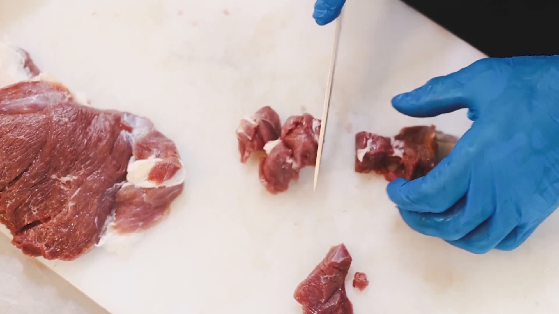 Hands cutting fresh beef into cubes on a board