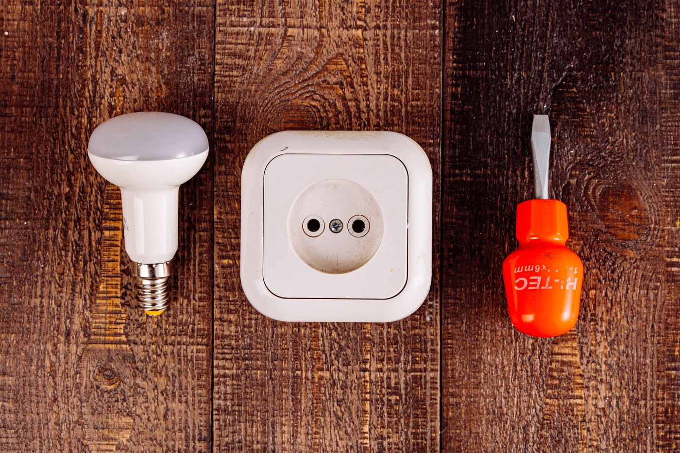 A bulb, socket and screwdriver on a wood surface