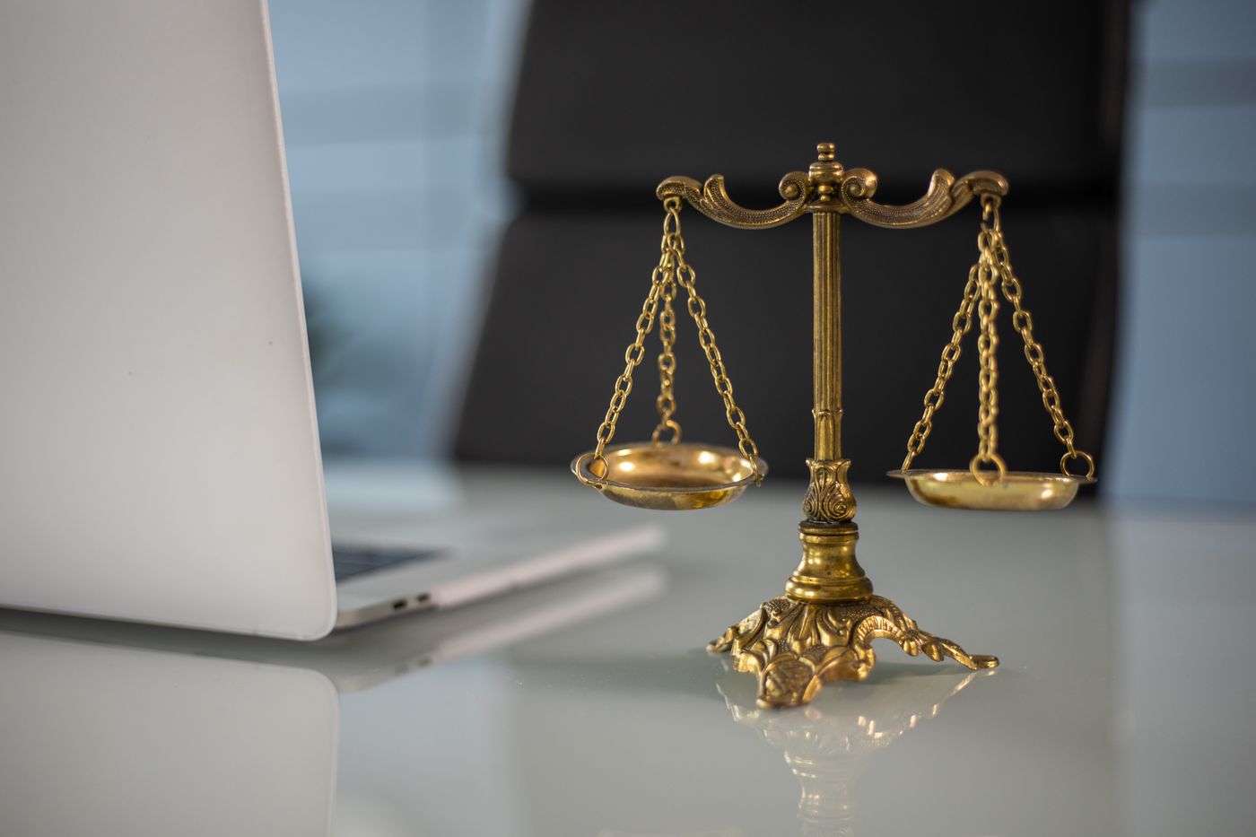 Brass scales of justice on a desk beside a laptop