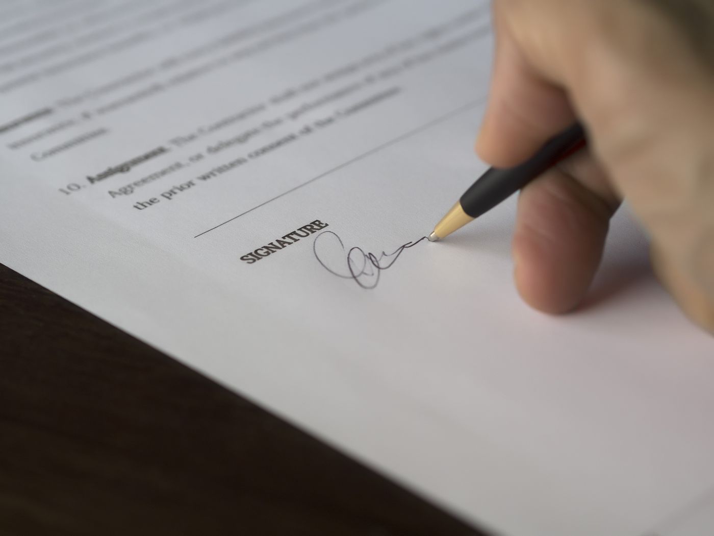 A hand signing a legal document at the signature line