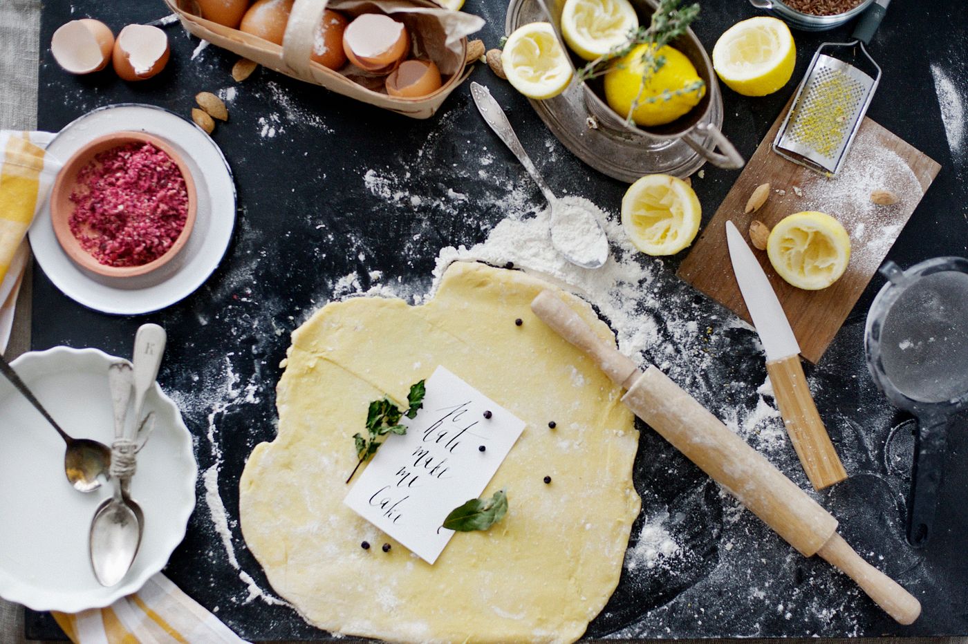 A floured bakehouse bench with rolled pastry, a rolling pin, eggs and lemons