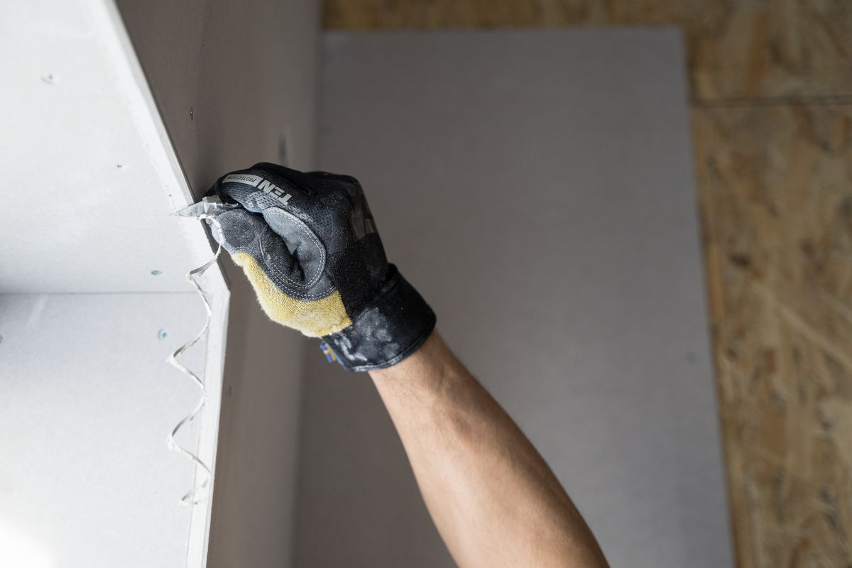 A gloved hand smoothing fresh plaster onto a repaired wall