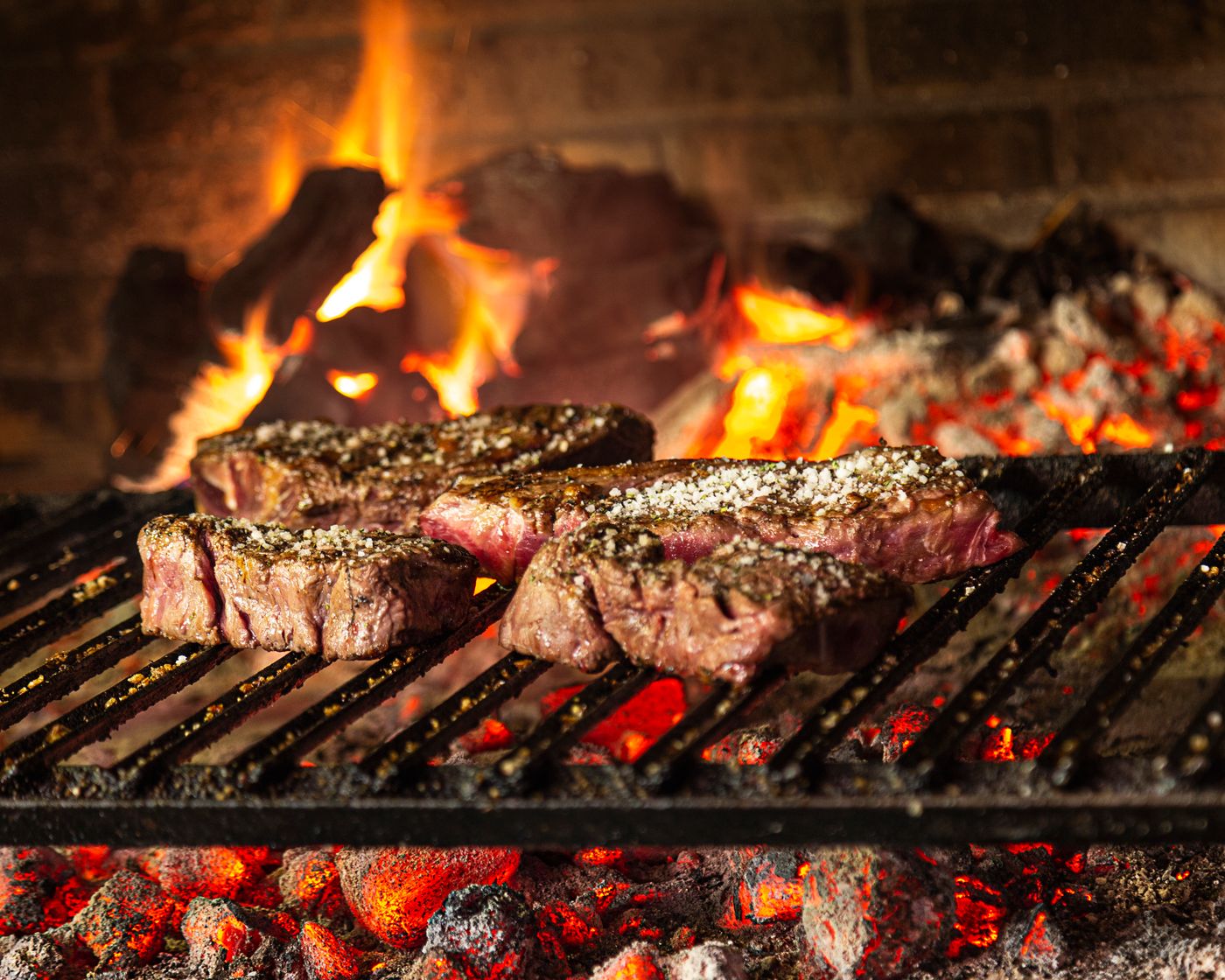 Cuts of meat cooking over open coals