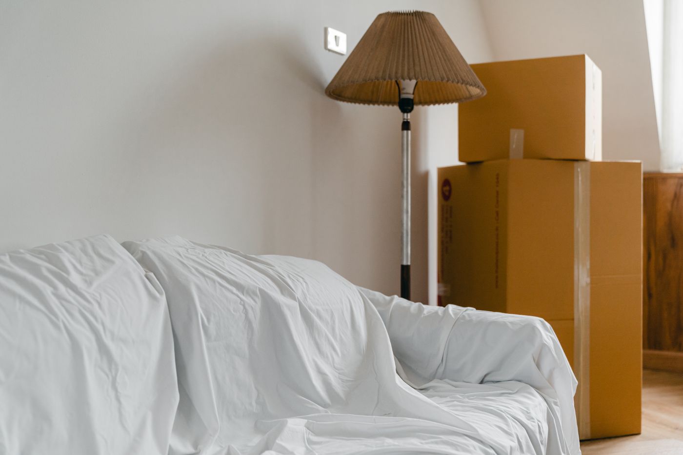 A sofa wrapped in a protective blanket beside packed cardboard boxes, mid-move