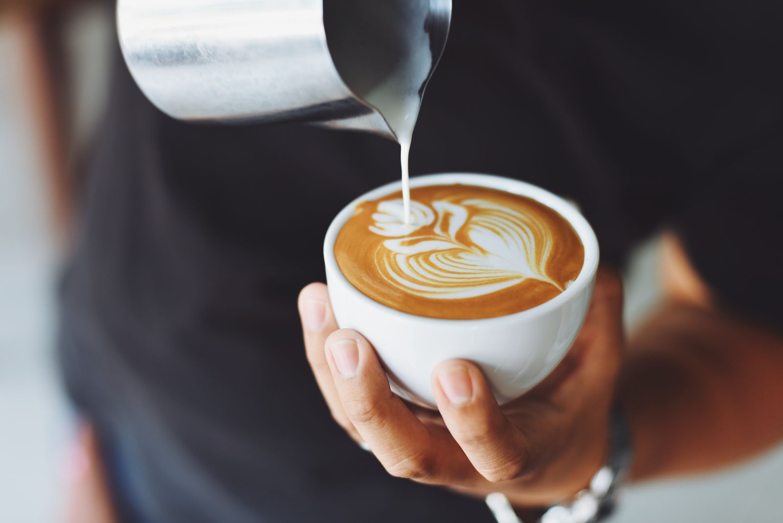 Steamed milk being poured into a flat white with rosetta latte art