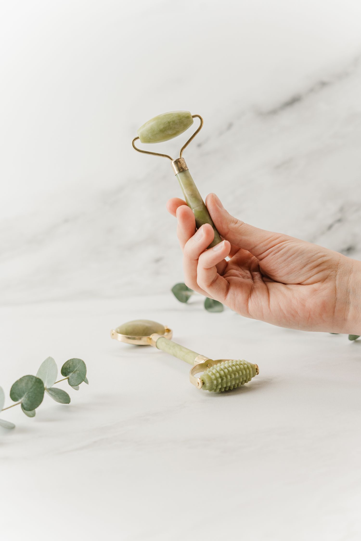 A hand holding a jade facial roller on marble