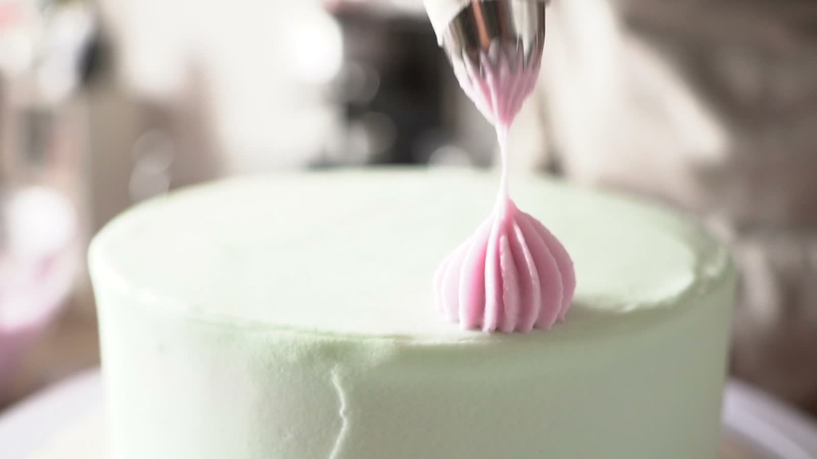 A piping bag setting a pink rosette onto a pale green cake